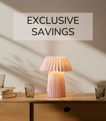 Nježna ružičasta stolna lampa na drvenom ormariću, okružena čašama i knjigama u toplom sunčevom svjetlu.